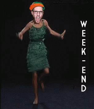 A Woman In A Green Dress Is Dancing In Front Of A Sign That Says Week End GIF