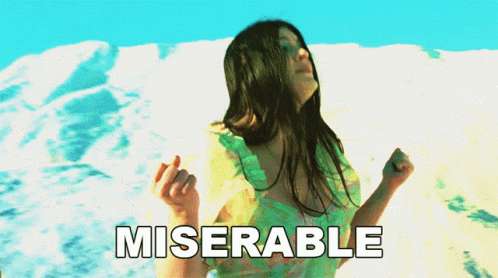 A Woman In A Green Dress Is Dancing In Front Of A Snowy Mountain And The Word Miserable Is Written Below Her GIF