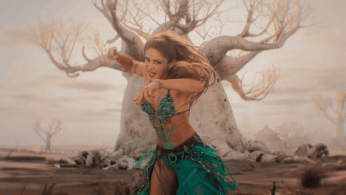 a woman in a green dress is dancing in front of a tree in the desert