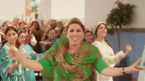 A Woman In A Green Dress Is Dancing With A Group Of Women In Blue Dresses . GIF
