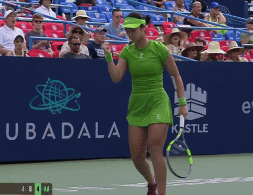 A Woman In A Green Dress Is Holding A Tennis Racquet In Front Of A Sign That Says Ubadala GIF