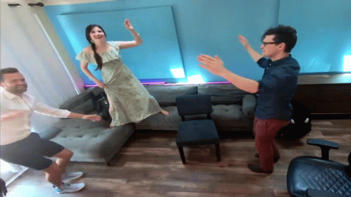 A Woman In A Green Dress Is Jumping In The Air While Two Men Watch GIF