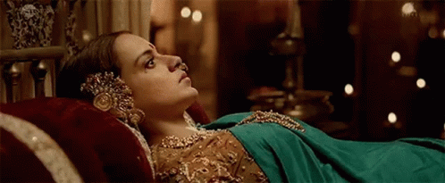 A Woman In A Green Dress Is Laying On A Bed With A Red Pillow . GIF