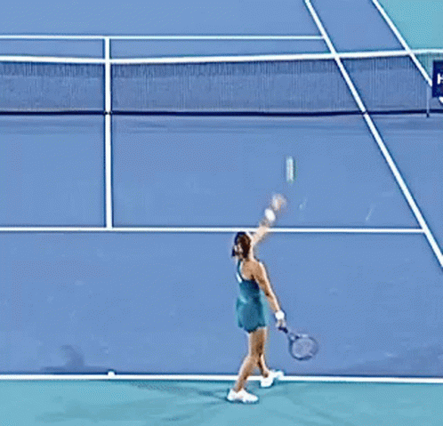 A Woman In A Green Dress Is Playing Tennis On A Court GIF