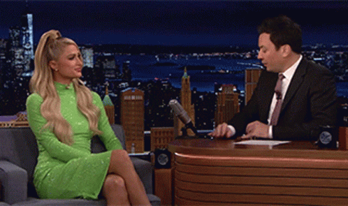 A Woman In A Green Dress Is Sitting In Front Of A Man In A Suit GIF