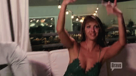 A Woman In A Green Dress Is Sitting On A Couch With Her Arms Outstretched . GIF