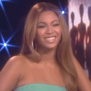 A Woman In A Green Dress Is Smiling And Looking At The Camera On A Stage . GIF