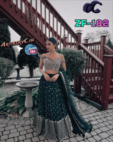 A Woman In A Green Dress Is Standing In Front Of A Staircase With Artistryc.in Written On The Bottom GIF