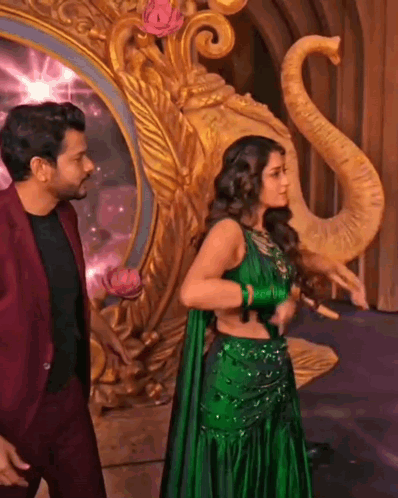 A Woman In A Green Dress Is Standing Next To A Man In A Red Suit . GIF