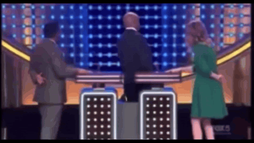 A Woman In A Green Dress Is Standing Next To A Man In A Suit GIF