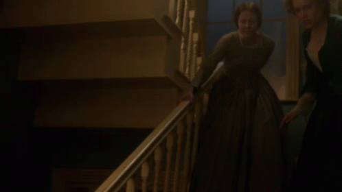 A Woman In A Green Dress Is Walking Down A Staircase GIF