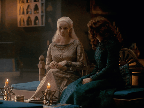 A Woman In A Green Dress Sits Next To A Woman In A White Dress GIF