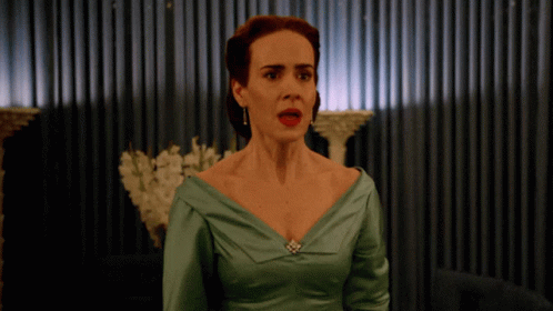 A Woman In A Green Dress Stands In Front Of A Curtain GIF