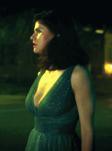 A Woman In A Green Dress With A Plunging Neckline Is Standing In Front Of A Yellow Sign GIF