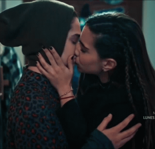 a woman in a green hat is kissing another woman on the forehead .