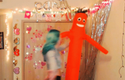 A Woman In A Green Head Scarf Stands Next To A Man In An Orange Balloon GIF