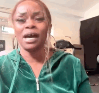 a woman in a green hoodie is making a funny face while standing in a room .
