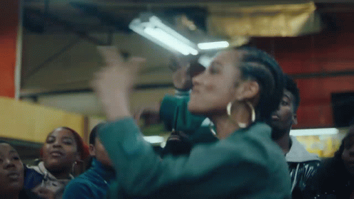 A Woman In A Green Jacket Is Dancing In Front Of A Crowd . GIF