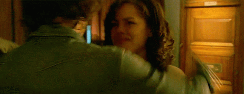 A Woman In A Green Jacket Is Hugging Another Woman In Front Of A Wooden Cabinet GIF
