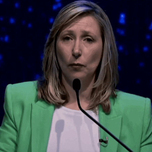 A Woman In A Green Jacket Is Talking Into A Microphone GIF