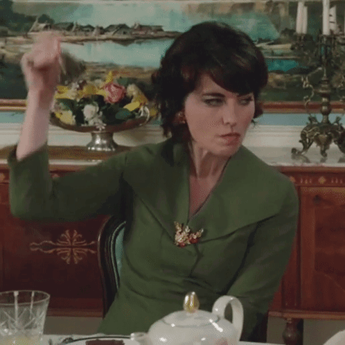 A Woman In A Green Jacket Sits At A Table GIF