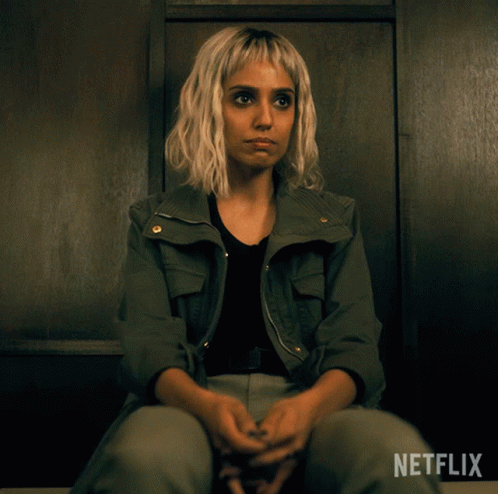 A Woman In A Green Jacket Sits In A Dark Room With Netflix Written On The Bottom GIF
