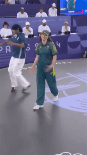 A Woman In A Green Jumpsuit Is Dancing With A Man In A Blue Shirt With The Number 4 On It GIF