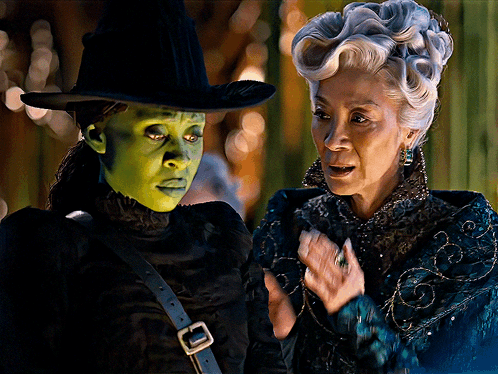 A Woman In A Green Mask Stands Next To Another Woman GIF