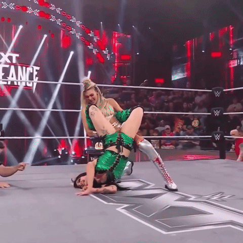 A Woman In A Green Outfit Is Doing A Flip In A Wrestling Ring With The Words Next Eance Behind Her GIF