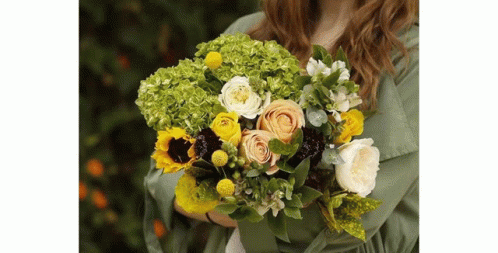 A Woman In A Green Shirt Is Holding A Bouquet Of Flowers . GIF