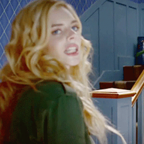 A Woman In A Green Shirt Is Standing In Front Of Stairs GIF