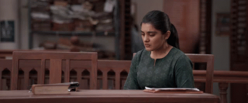 a woman in a green shirt sits at a wooden table