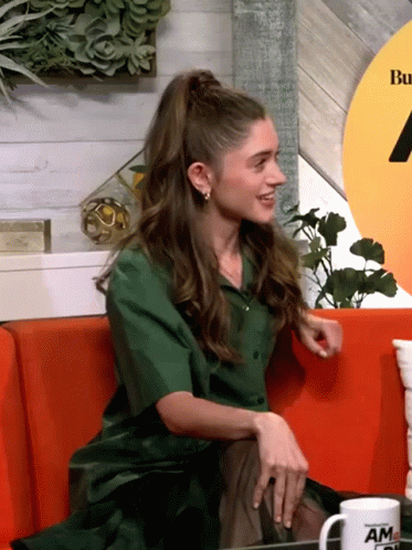A Woman In A Green Shirt Sits On A Red Couch Next To A Mug That Says Am GIF