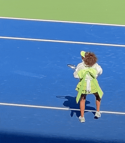 A Woman In A Green Skirt Is Holding A Tennis Racquet On A Tennis Court GIF