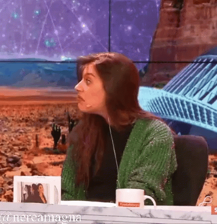 A Woman In A Green Sweater Is Sitting At A Table With A Mug That Says ' Nevada ' On It GIF
