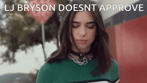 A Woman In A Green Sweater Is Standing In Front Of A Red Sign That Says " Lj Bryson Doesnt Approve " GIF