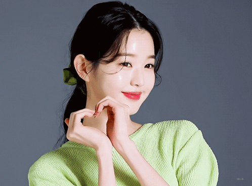 A Woman In A Green Sweater Making A Heart With Her Hands GIF