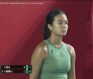 A Woman In A Green Tank Top Is Standing In Front Of A Red Background . GIF