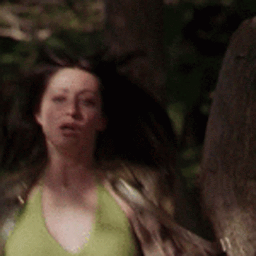 A Woman In A Green Tank Top Is Walking Through A Forest . GIF