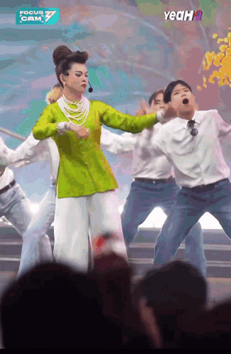 a woman in a green top and white pants is dancing in front of a crowd and a sign that says yeah