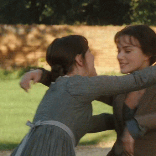 A Woman In A Grey Dress Is Hugging Another Woman In A Brown Jacket GIF