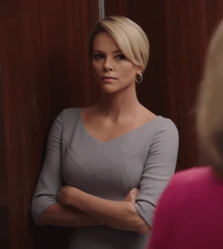 A Woman In A Grey Dress Stands With Her Arms Crossed Looking At Another Woman In A Pink Shirt GIF