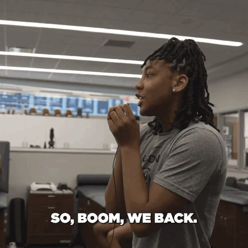 A Woman In A Grey Shirt Is Talking Into A Microphone With The Words So Boom We Back Written Below Her GIF