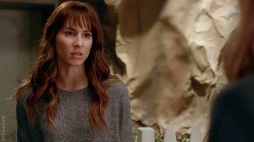 A Woman In A Grey Sweater Is Looking At Another Woman In Front Of A Wall Of Crumpled Paper . GIF