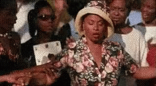 A Woman In A Hat Is Standing In A Crowd Of People . GIF