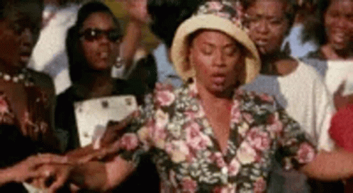 A Woman In A Hat Is Standing In Front Of A Crowd Of People Holding Hands . GIF