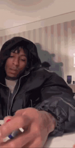 A Woman In A Hooded Jacket Is Sitting On A Bed And Holding A Marker . GIF