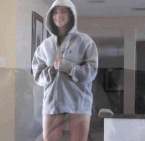 A Woman In A Hoodie Is Standing In A Hallway . GIF