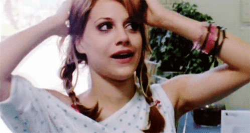 A Woman In A Hospital Gown Is Holding Her Hair In Pigtails And Making A Funny Face . GIF