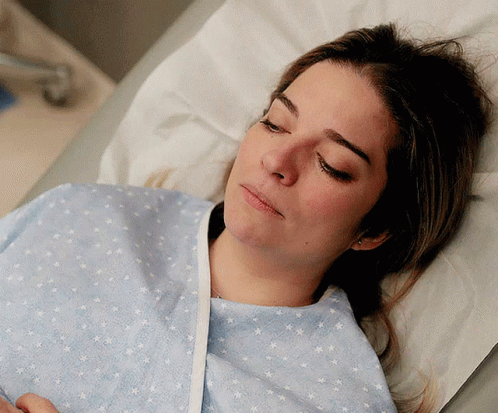 A Woman In A Hospital Gown Is Laying In A Bed With Her Eyes Closed GIF